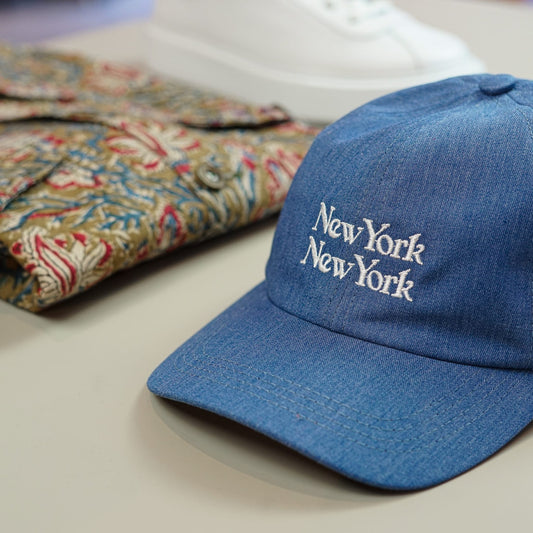 A photo of a blue New York cap and Corridor paisley printed jacket. on a white table.