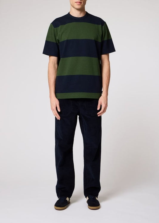 A model wearing a short-sleeve crewneck t-shirt with horizontal stripes in dark green and navy blue, paired with dark pants and dark slip-on shoes, against a plain light gray studio background.