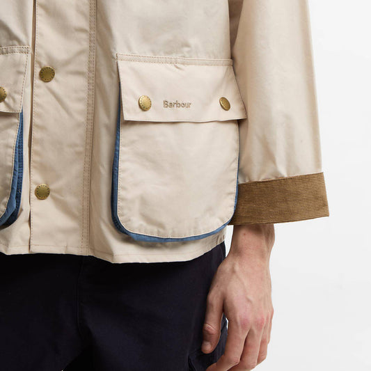 Close-up of a beige jacket with gold buttons and blue lining, featuring the Barbour brand logo.