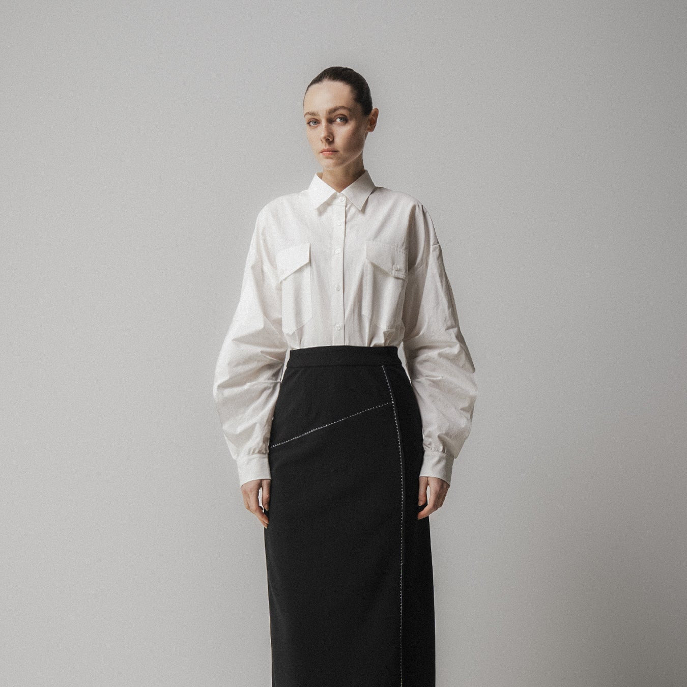 Person wearing a white blouse and black skirt against a plain background