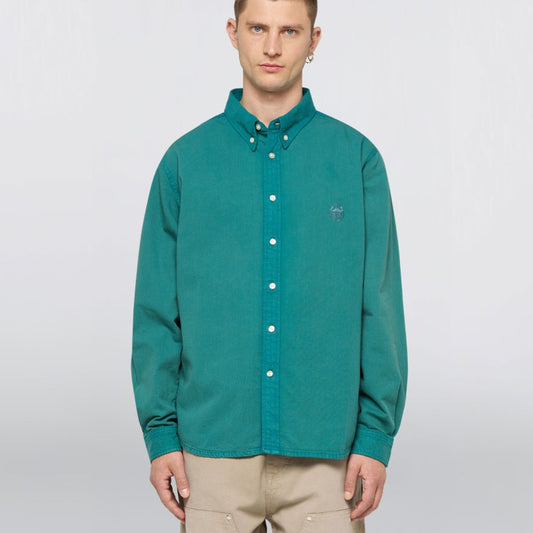 Man wearing a teal button-up shirt with a small logo on a white background