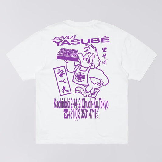 A white short-sleeve T-shirt shown flat against a light gray background, featuring a large purple graphic print on the front with the text '2024 YASUBÉ' and additional Japanese text and illustration details.