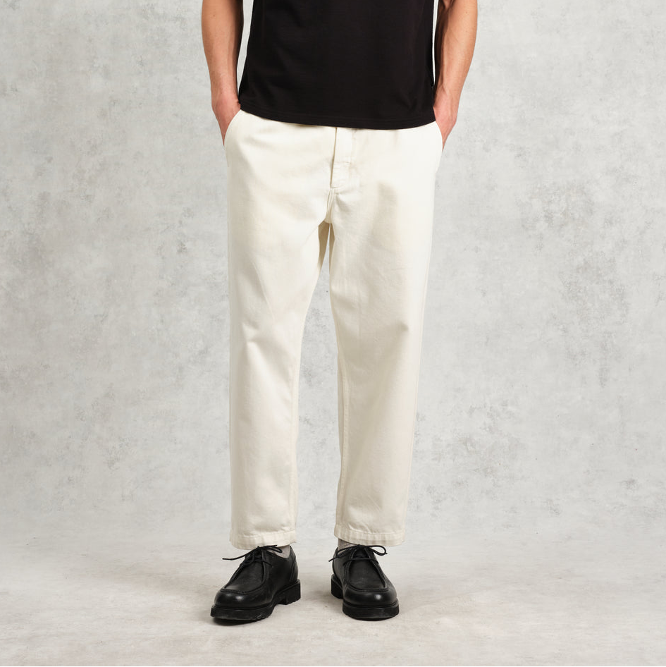 Man wearing a black t-shirt, white pants, and black shoes against a gray background