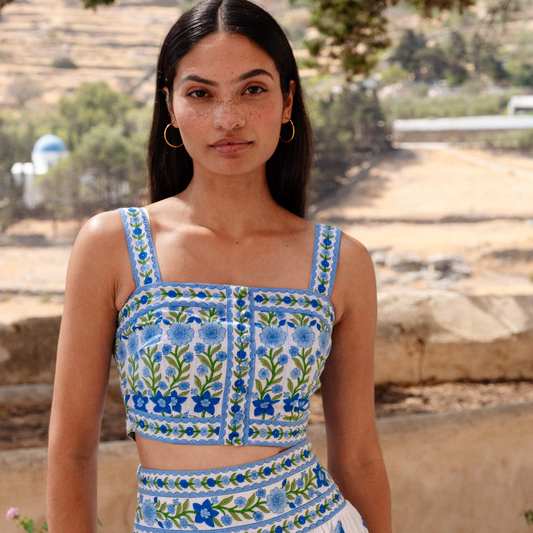 Woman wearing a blue and white embroidered top and skirt outdoors.