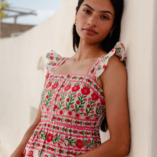 Woman wearing a floral dress leaning against a white wall.